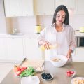 Nice girl is cooking in kitchen. She is mixing ingredients for salad in bowl. Girl is calm and concentrated