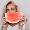 Close-up portrait of girl with gray eyes eating watermelon. Indoor photo of spectacular caucasian lady with long hairstyle enjoying fruits.