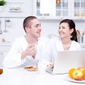 Happiness of young loving couple sitting in the kitchen with laptop